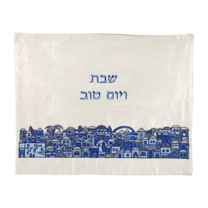 כיסוי חלה לשבת משולב בבדים ורקמות שונות בגווני כחול ותכלת על רקע שמנת, עם עיטורי נוף עירוני וכיתוב שבת ויום טוב