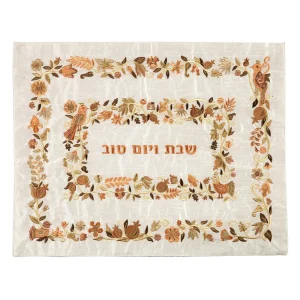 כיסוי חלה לשבת משולב בבדים ורקמות שונות בגווני חום, ברונזה וזהב על רקע שמנת, עם מסגרות, עיטורי ציפורים, פרחים ורימונים וכיתוב שבת ויום טוב