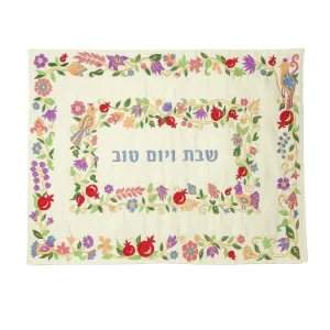 כיסוי חלה לשבת משולב בבדים ורקמות שונות בגוונים צבעוניים על רקע שמנת, עם מסגרות, עיטורי ציפורים, פרחים ורימונים וכיתוב שבת ויום טוב