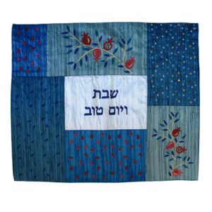כיסוי חלה לשבת משולב בבדים ורקמות שונות בגווני כחול ותכלת עם עיטורי רימונים אדומים וכיתוב שבת ויום טוב