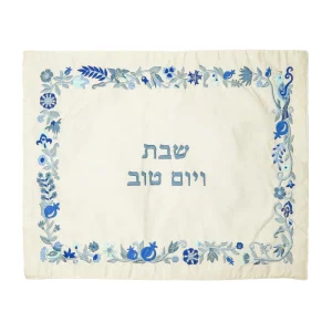 כיסוי חלה לשבת משולב בבדים ורקמות שונות בגווני כחול ותכלת על רקע שמנת, עם מסגרת, עיטורי ציפורים, פרחים ורימונים וכיתוב שבת ויום טוב