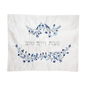 כיסוי חלה לשבת משולב בבדים ורקמות שונות בגווני כחול, תכלת וכסף על רקע שמנת, עם עיטורי ציפורים, פרחים וענפים וכיתוב שבת ויום טוב