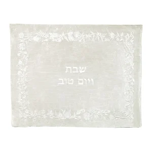 כיסוי חלה לשבת משולב בבדים ורקמות שונות בגווני לבן ושמנת מונוכרומטיים, עם מסגרת, עיטורי פרחים ועלים וכיתוב שבת ויום טוב
