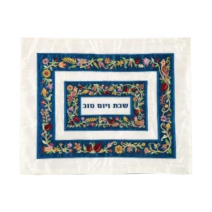 כיסוי חלה לשבת משולב בבדים ורקמות שונות בגוונים צבעוניים על רקע שמנת, עם מסגרות כחולות, עיטורי ציפורים, פרחים ורימונים וכיתוב שבת ויום טוב
