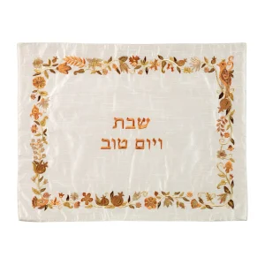 כיסוי חלה לשבת משולב בבדים ורקמות שונות בגווני חום, ברונזה וזהב על רקע שמנת, עם מסגרת, עיטורי ציפורים, פרחים ורימונים וכיתוב שבת ויום טוב