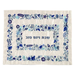 כיסוי חלה לשבת משולב בבדים ורקמות שונות בגווני כחול ותכלת על רקע שמנת, עם מסגרות, עיטורי ציפורים, פרחים ורימונים וכיתוב שבת ויום טוב