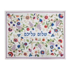 כיסוי חלה לשבת משולב בבדים ורקמות שונות בגוונים צבעוניים על רקע שמנת, עם מסגרת סגולה, עיטורי אשכולות ענבים, פרחים ועלים וכיתוב שלום עליכם